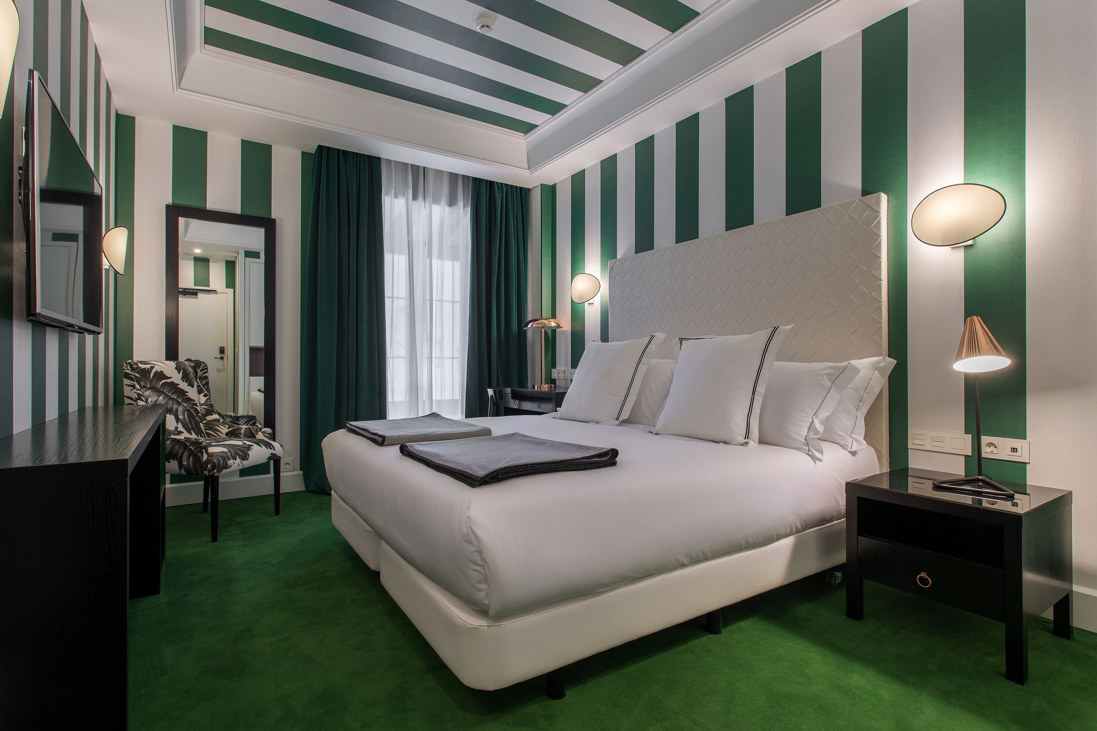 A hotel room with a large bed, two bedside tables, a chair, a desk, and a mirror.