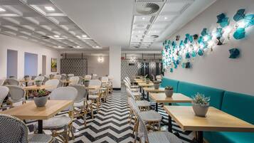 Un comedor moderno con mesas y sillas de madera, plantas en macetas y un suelo estampado.
