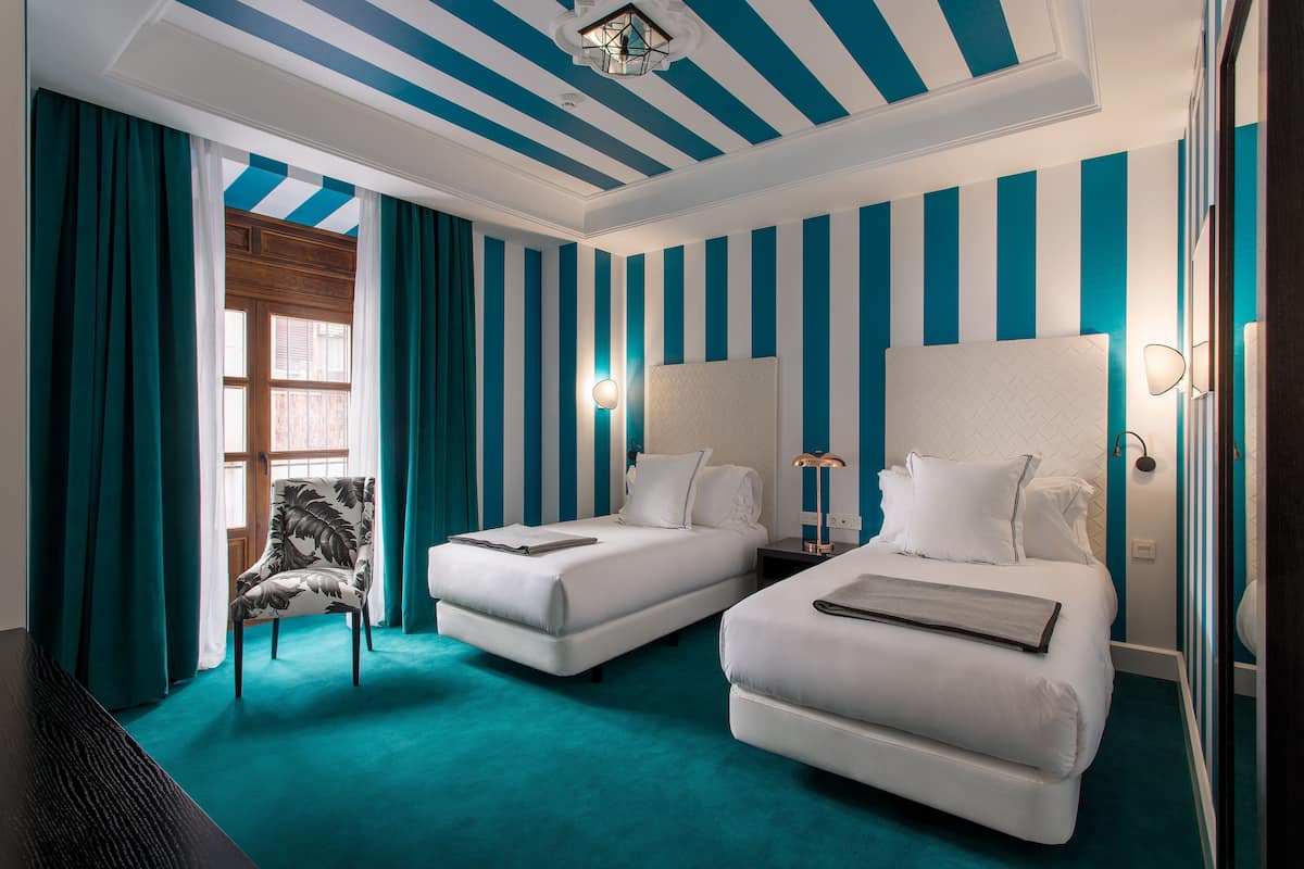 Una habitación de hotel con dos camas, una silla y un amplio ventanal con cortinas.