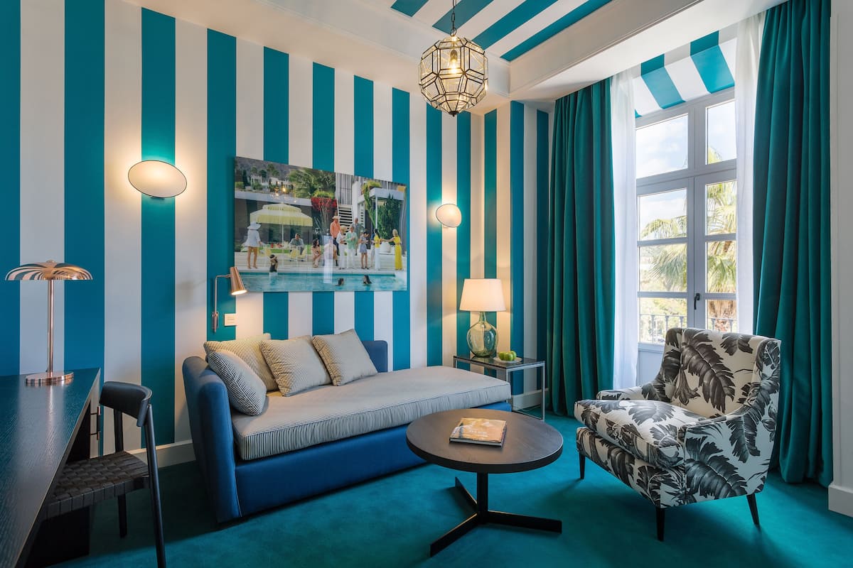 Una habitación con pared azul y blanca a rayas, un sofá, una silla, una mesa y una ventana con cortinas.