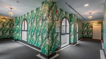 Un pasillo con paredes de estampado de hojas verdes, una lámpara en forma de estrella y una puerta con el símbolo de número.