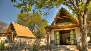 A traditional house with a thatched roof, surrounded by a garden with various plants and a large tree. - Thamalakane River Lodge (Maun)