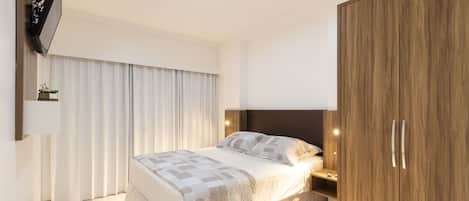 A modern bedroom with a bed, a wooden wardrobe, a bedside table, and a TV mounted on the wall.