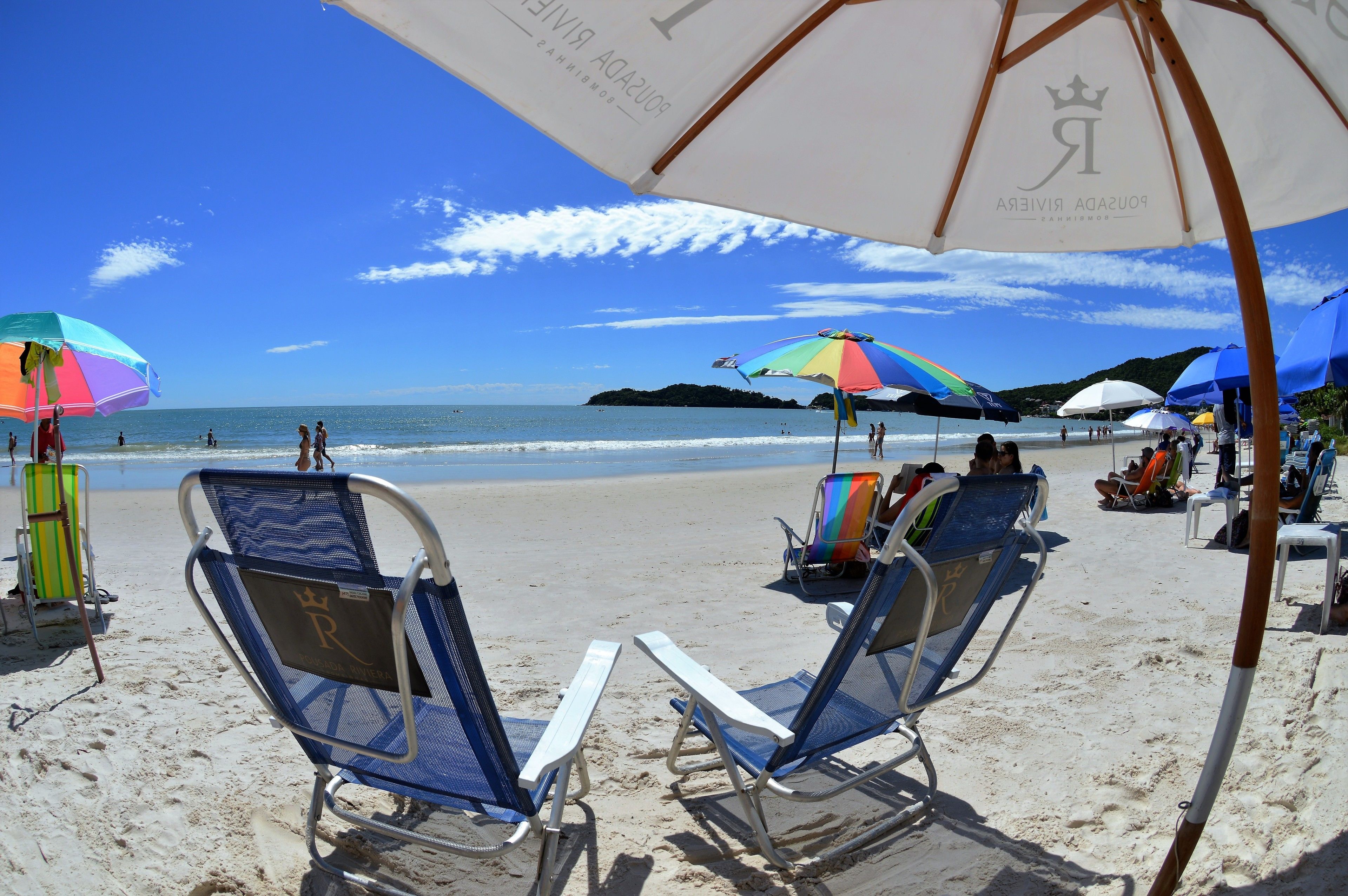 A beach with sun loungers and umbrellas, a clear sky, and the ocean in the background.