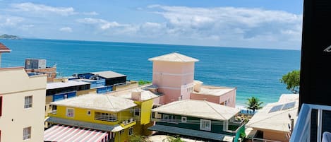 A coastal town with colorful buildings, a clear blue sky, and the sea in the background.