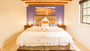 Un dormitorio con una cama grande, vigas de madera en el techo, un cuadro de atardecer y dos lámparas de noche.