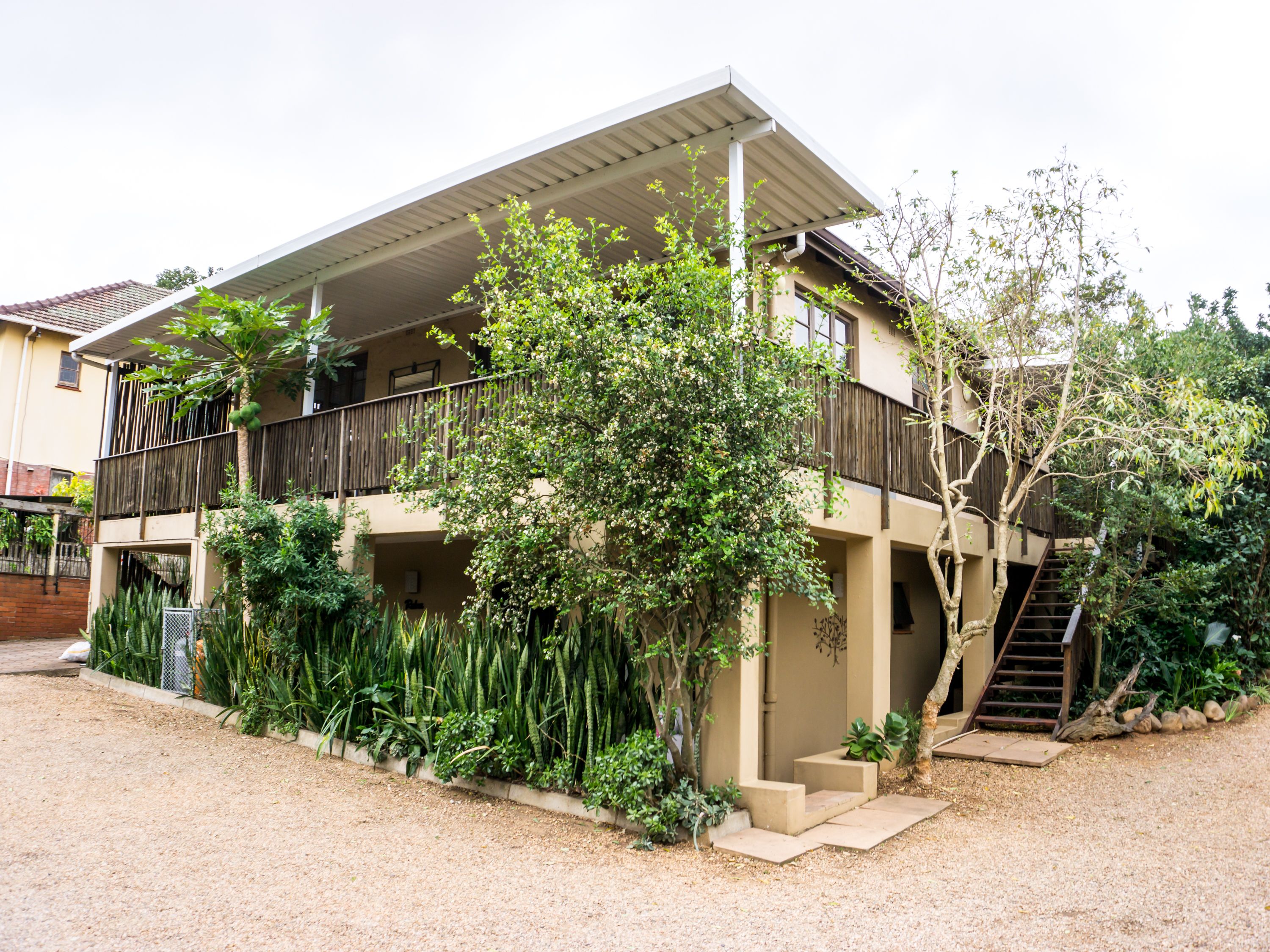 A two-story house with a balcony, surrounded by lush greenery.