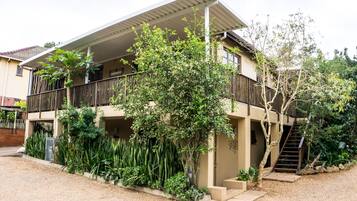 A two-story house with a balcony, surrounded by lush greenery.