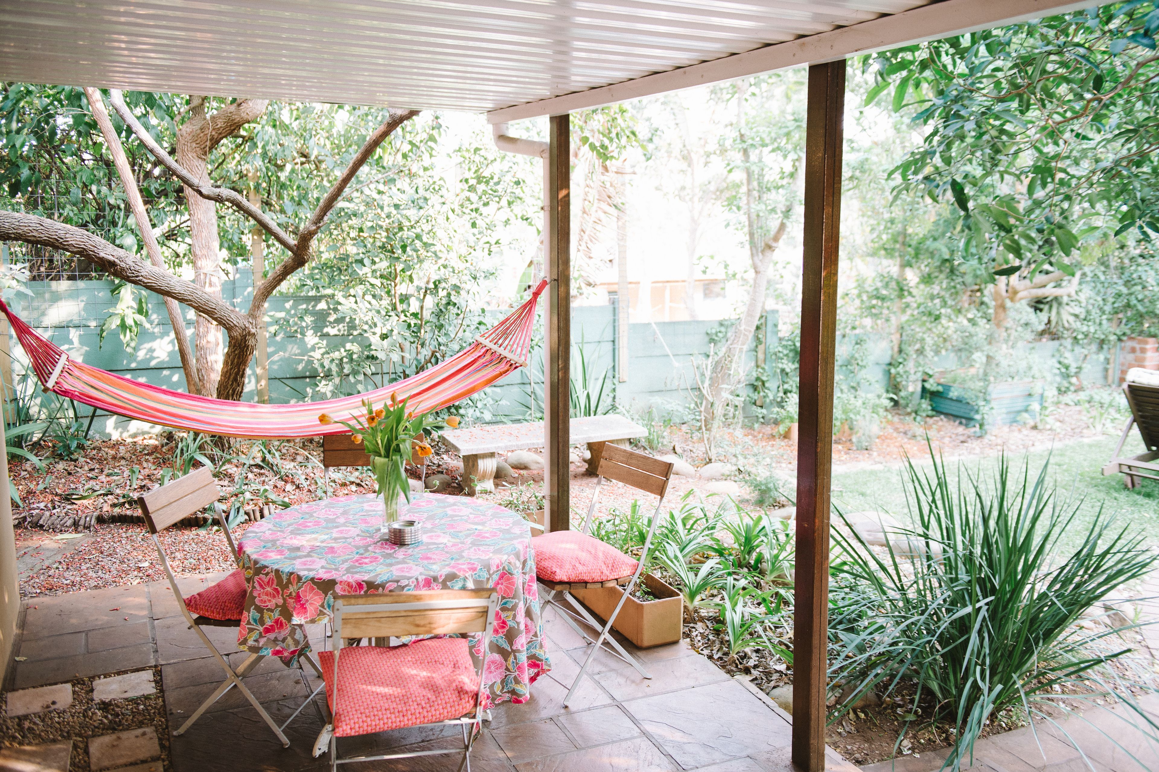 Um pátio com mesa e cadeiras, uma rede e um jardim com diversas plantas.