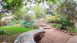 Un sendero en un jardín con un banco de mosaico, rodeado de diversas plantas y una valla de madera.