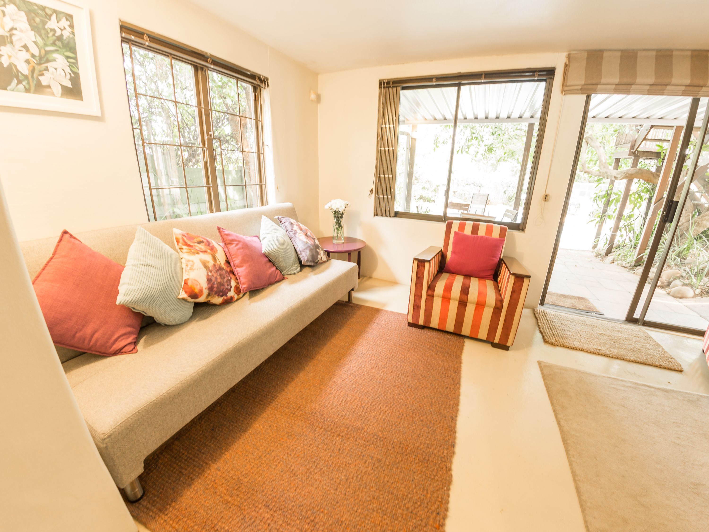 A living room with a beige sofa, colorful cushions, a striped armchair, and a small table with a vase.