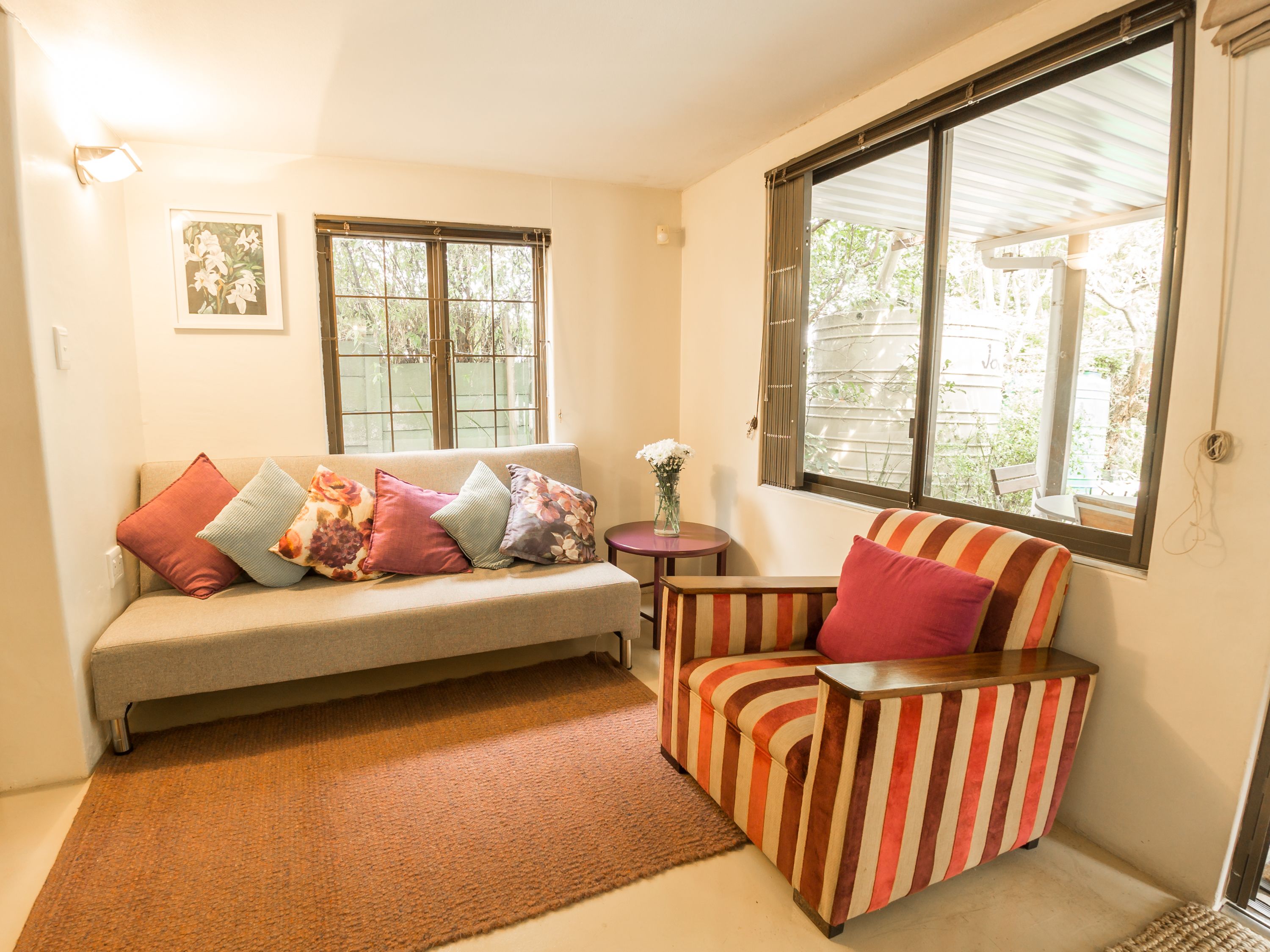 Un salón acogedor con sofá, un sillón a rayas, una mesita y una ventana con vistas al verdor.