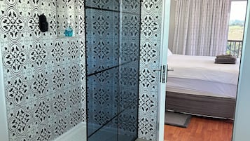 Un bagno moderno con cabina doccia in vetro, carta da parati decorata e vista su una camera da letto con un letto e tende.