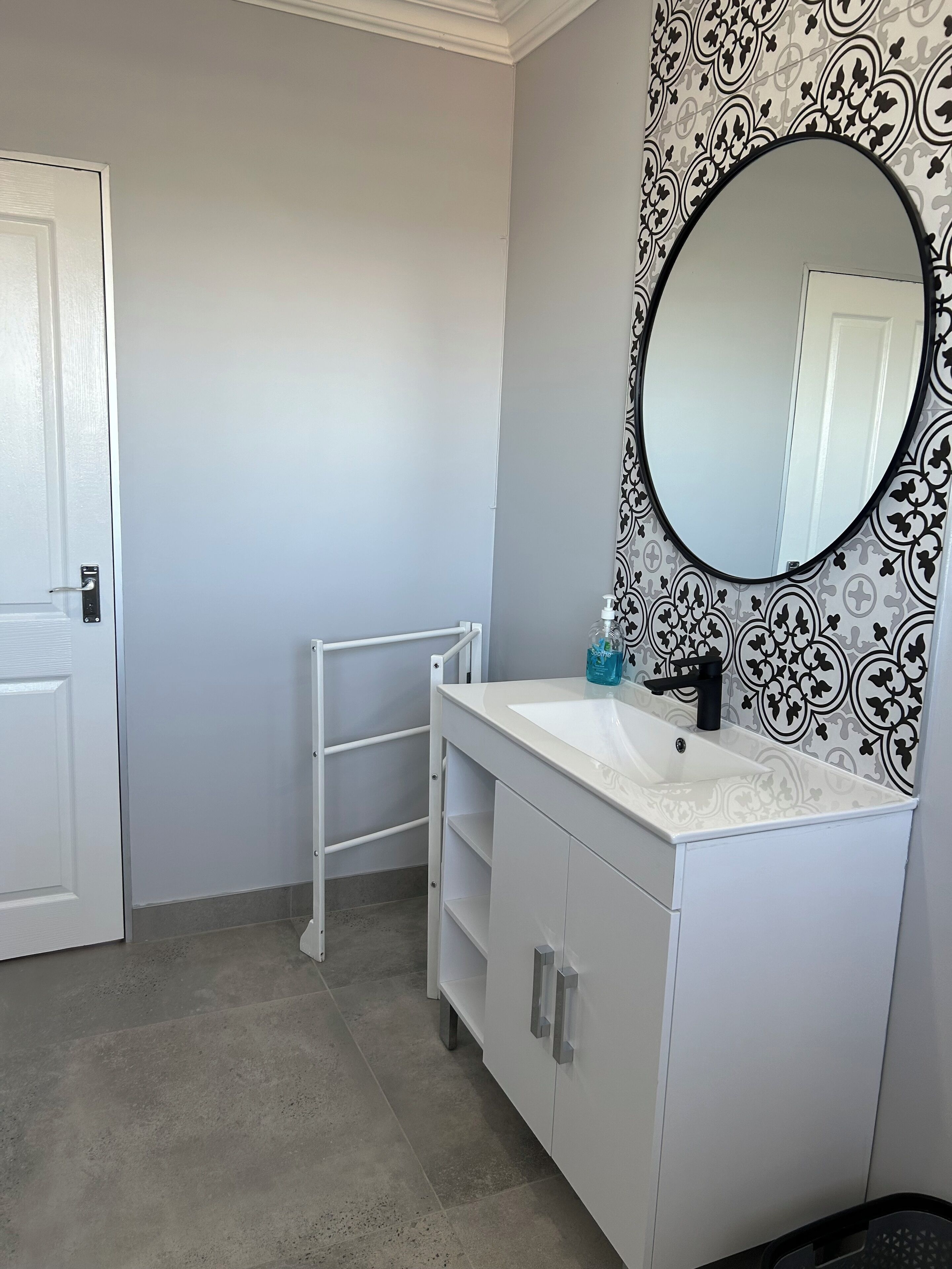 Une salle de bain avec un meuble-lavabo blanc, un robinet noir, un miroir à cadre noir et un mur à motifs.