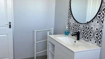 Une salle de bain avec un meuble-lavabo blanc, un robinet noir, un miroir à cadre noir et un mur à motifs.