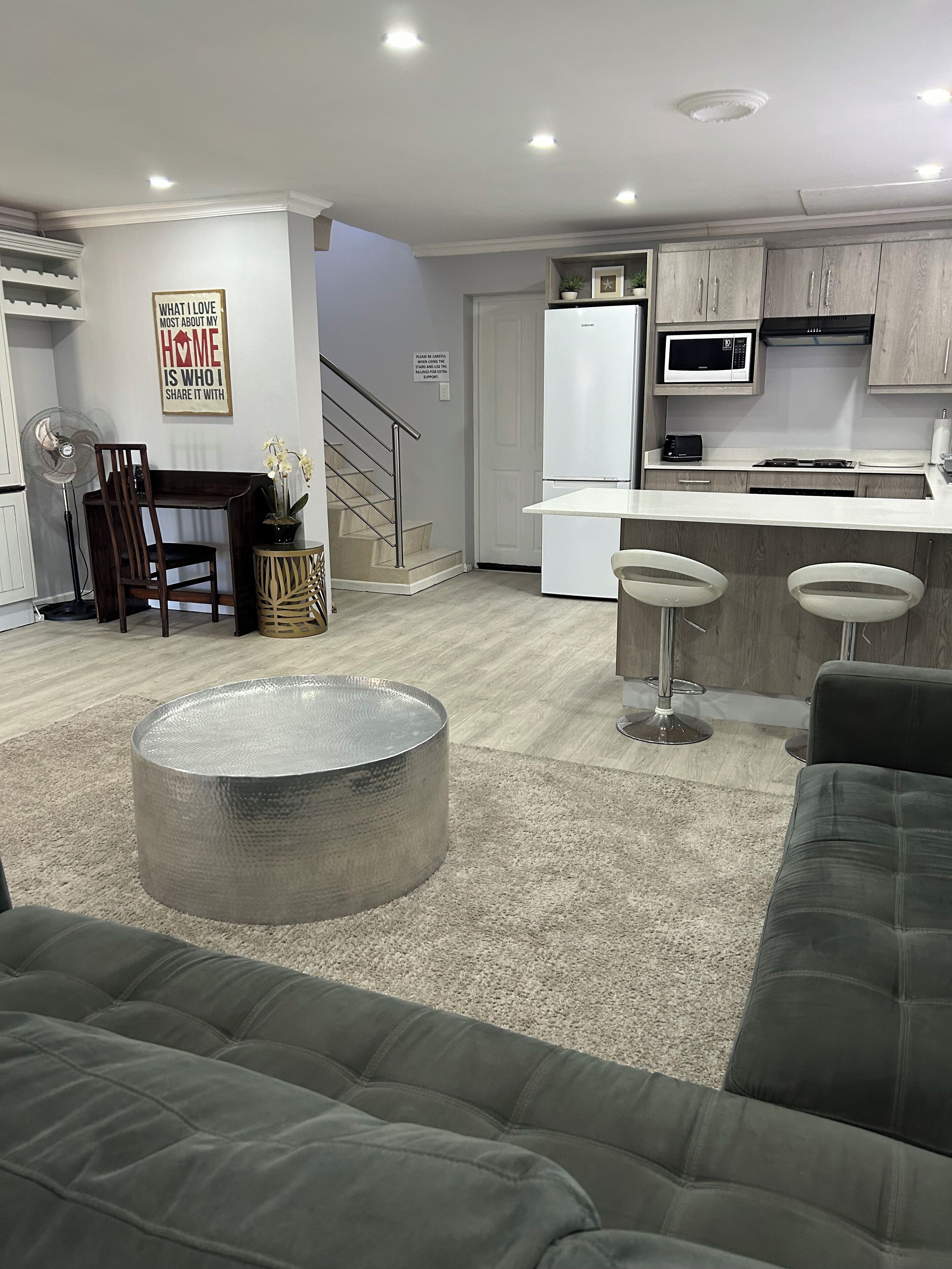 A modern kitchen with a microwave, stove, and bar stools. There is a dining area with a table and chairs, and a staircase leading to another level.