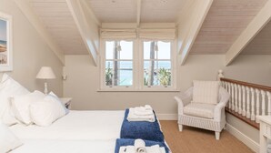 Een slaapkamer met een groot bed, een stoel, een raam met uitzicht op zee en een houten plafond.