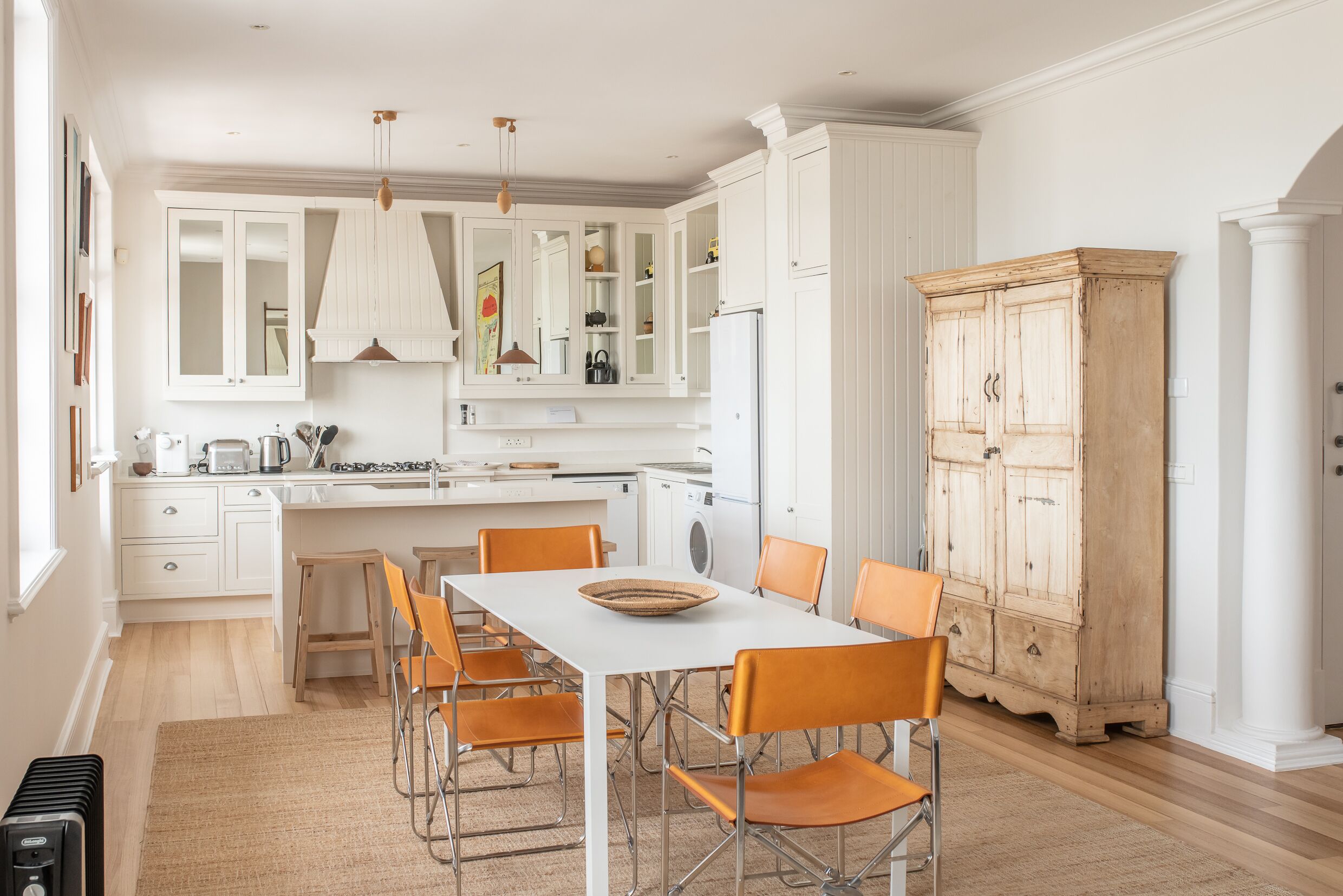 Une cuisine moderne avec des meubles blancs, un îlot central et des chaises orange.