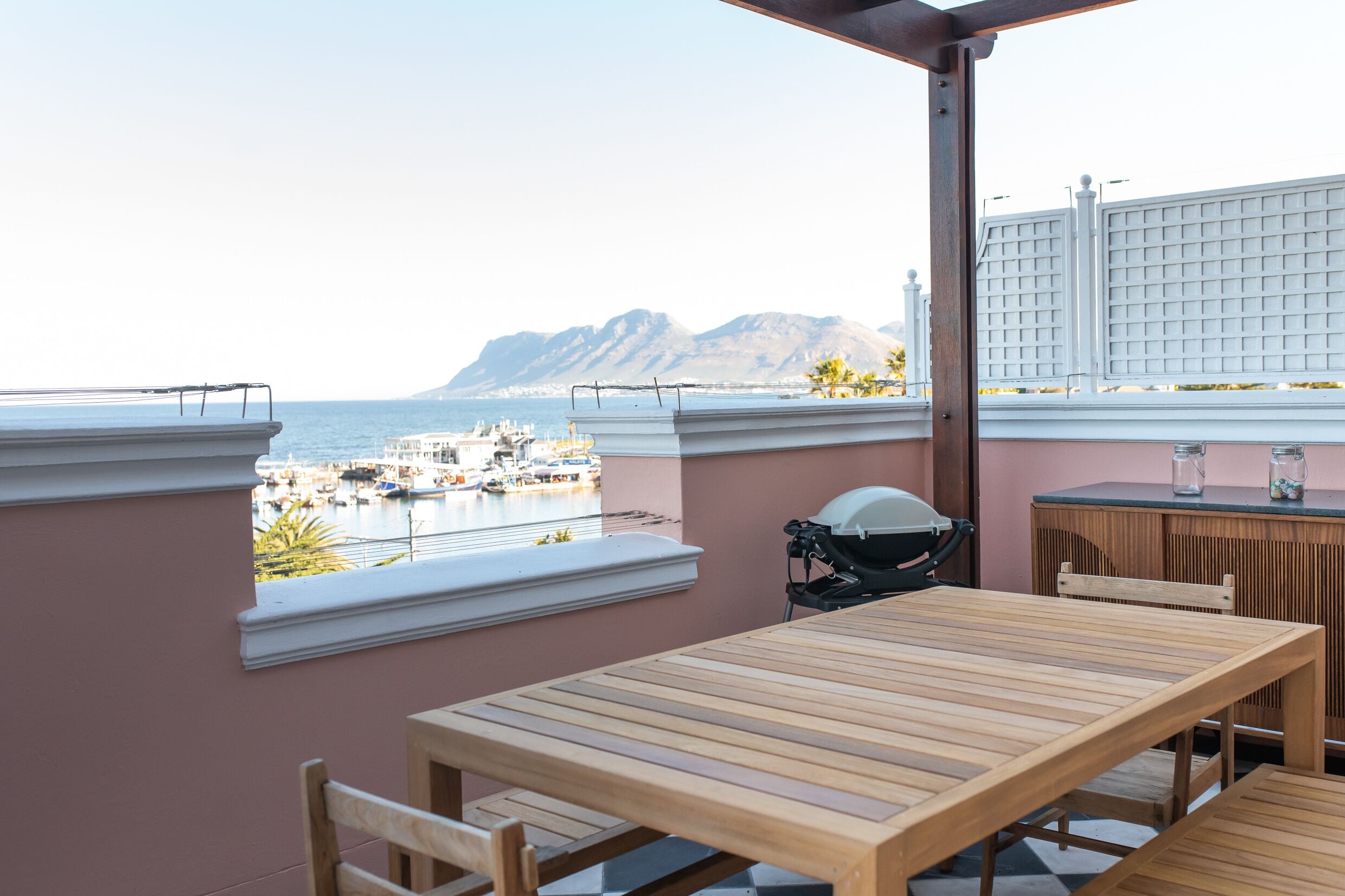 Una mesa y sillas de madera en un balcón con vista al mar y a las montañas.