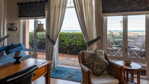 Een kamer met uitzicht op zee, een bank, een stoel, een tafel en een lamp.