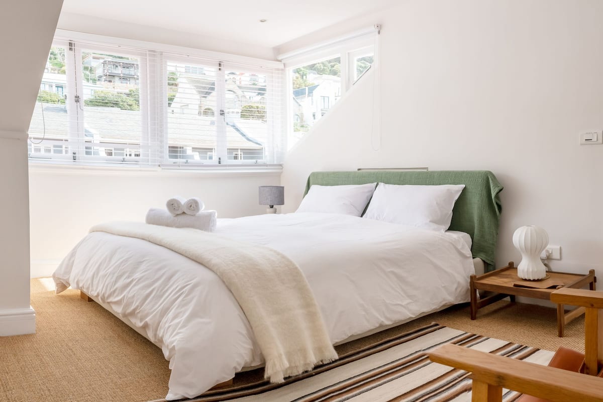 Een slaapkamer met een groot bed, uitzicht naar buiten en een klein tafeltje met een lamp.