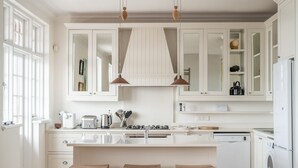 Een moderne keuken met witte kasten, een centraal eiland met krukken, een inbouw vaatwasser en een fornuis.
