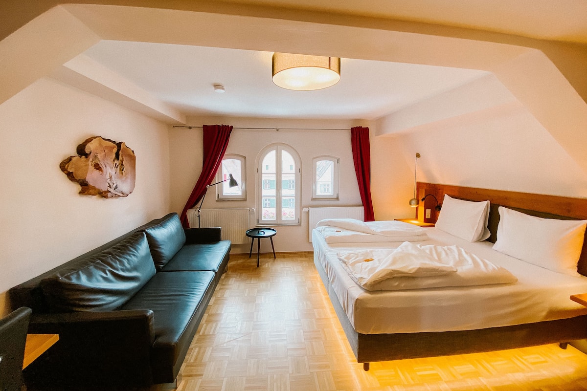 A room with a bed, a sofa, a small table, and a window with curtains.