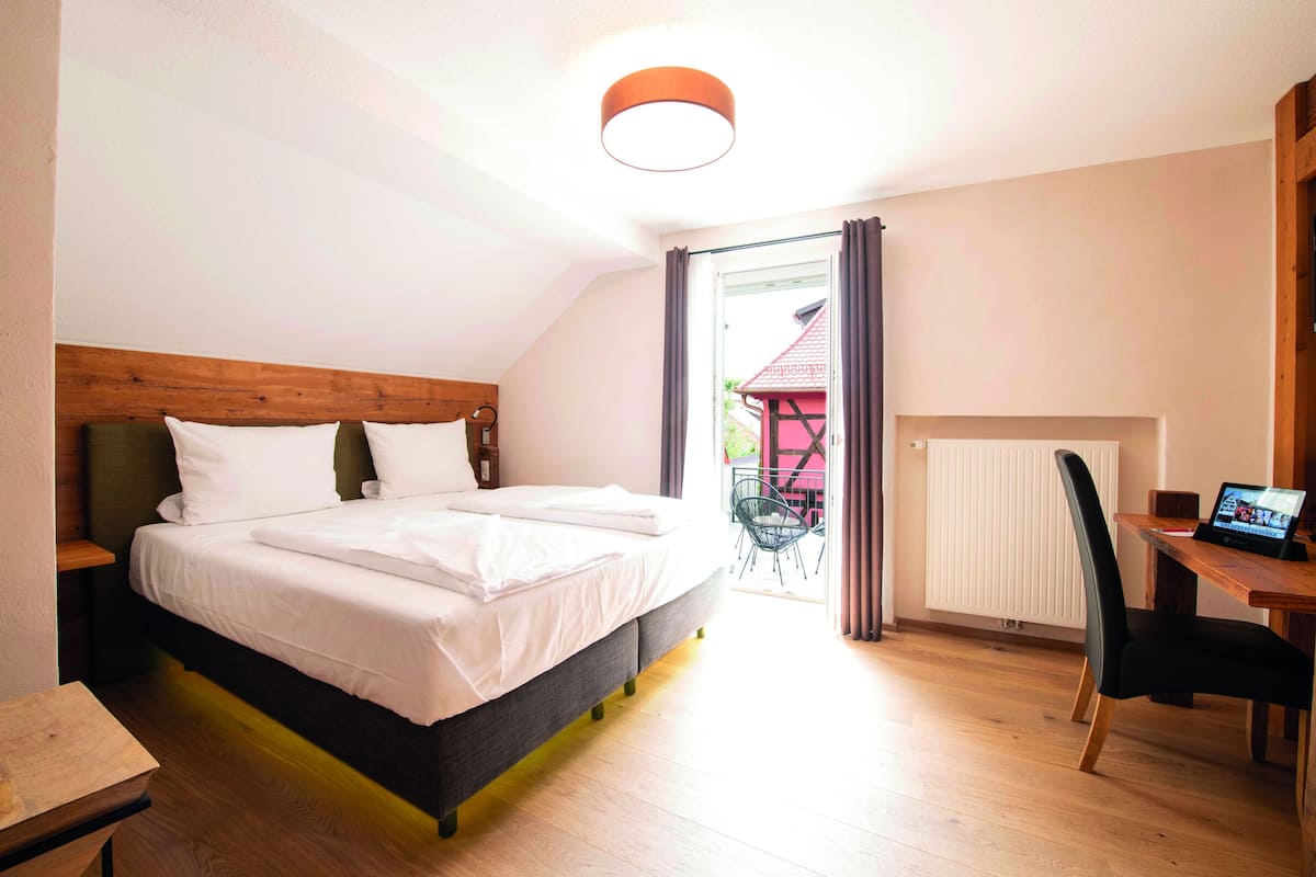 A bedroom with a bed, a wooden headboard, a desk with a chair, and a view of the outside.