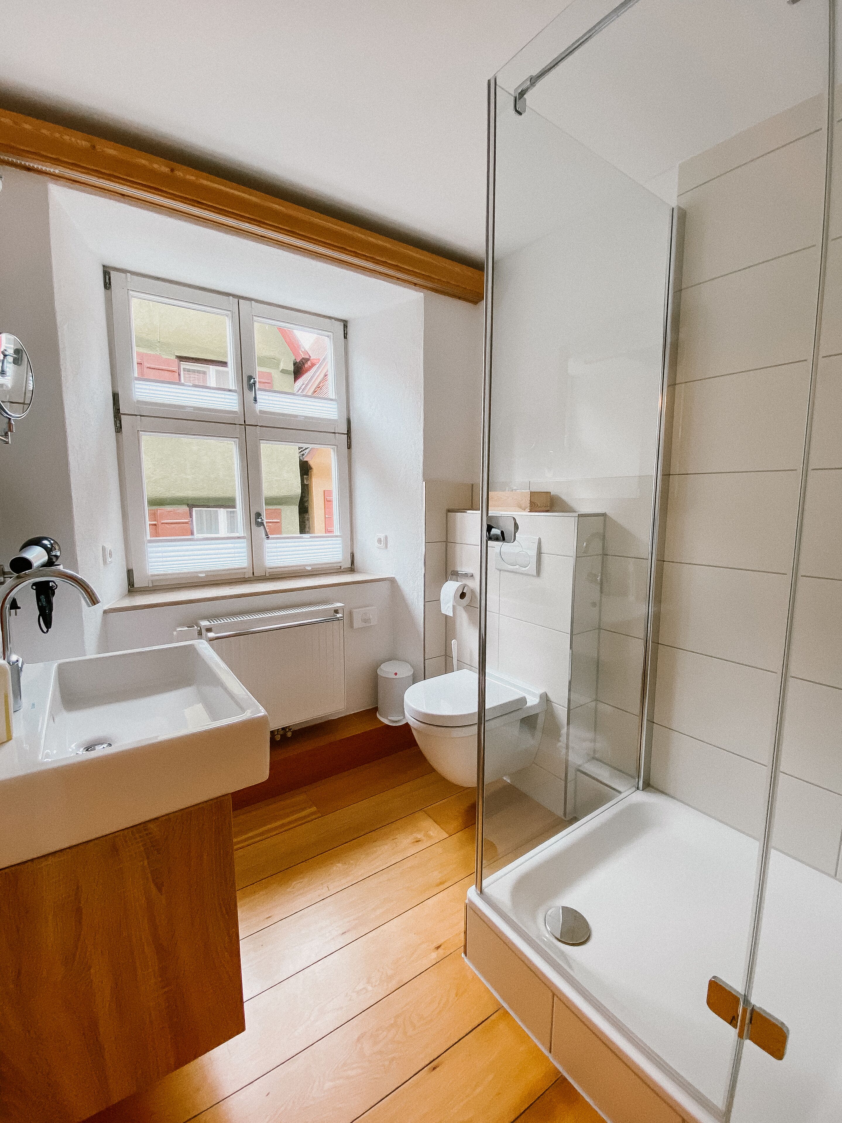 Un baño moderno con ducha envuelta en vidrio, un lavamanos, un inodoro y una ventana con persianas.