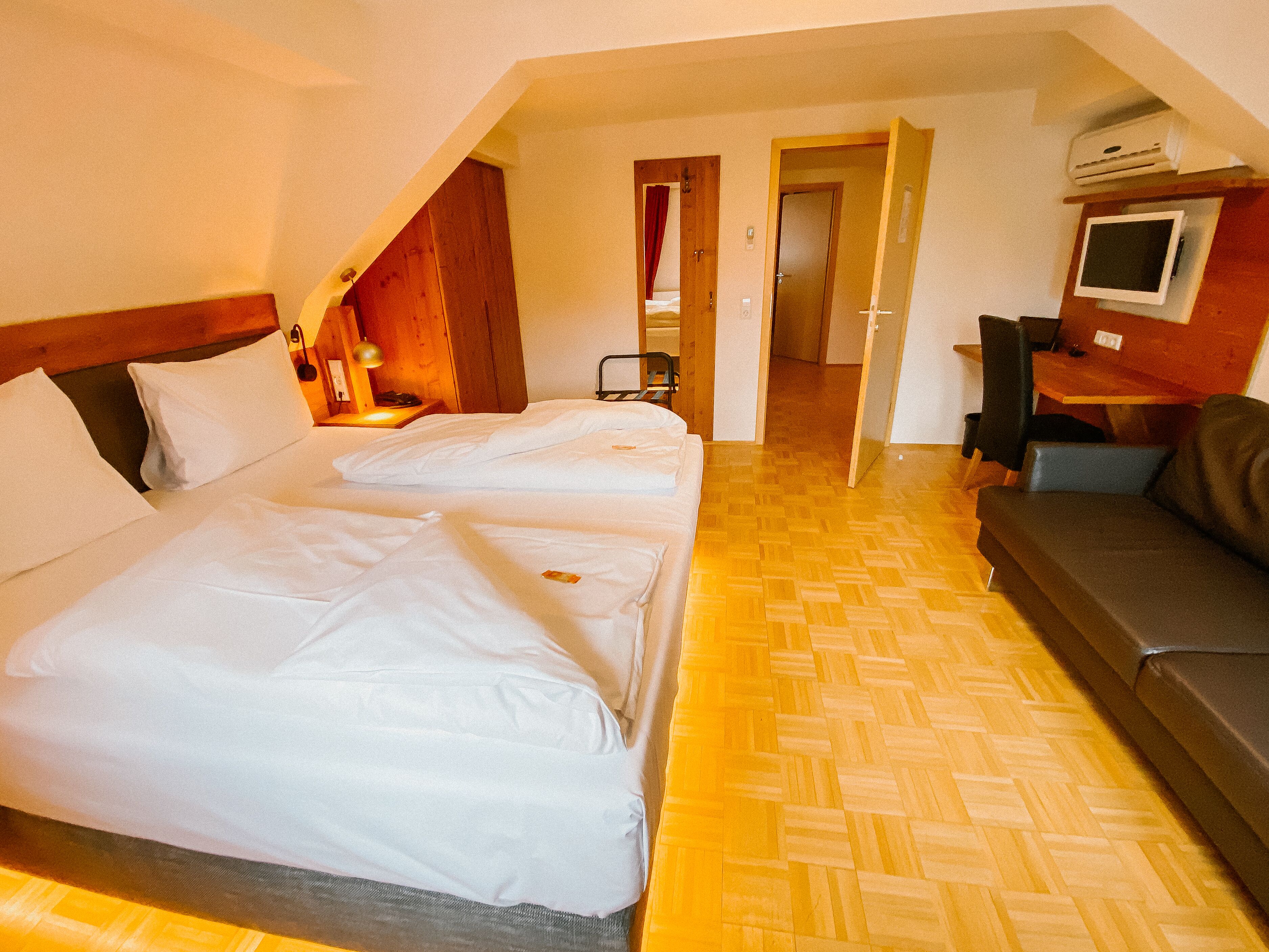 A hotel room with two beds, a sofa, a TV, and a desk.