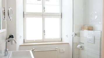 A modern bathroom with a wooden floor, white fixtures, a window, and a glass shower enclosure.