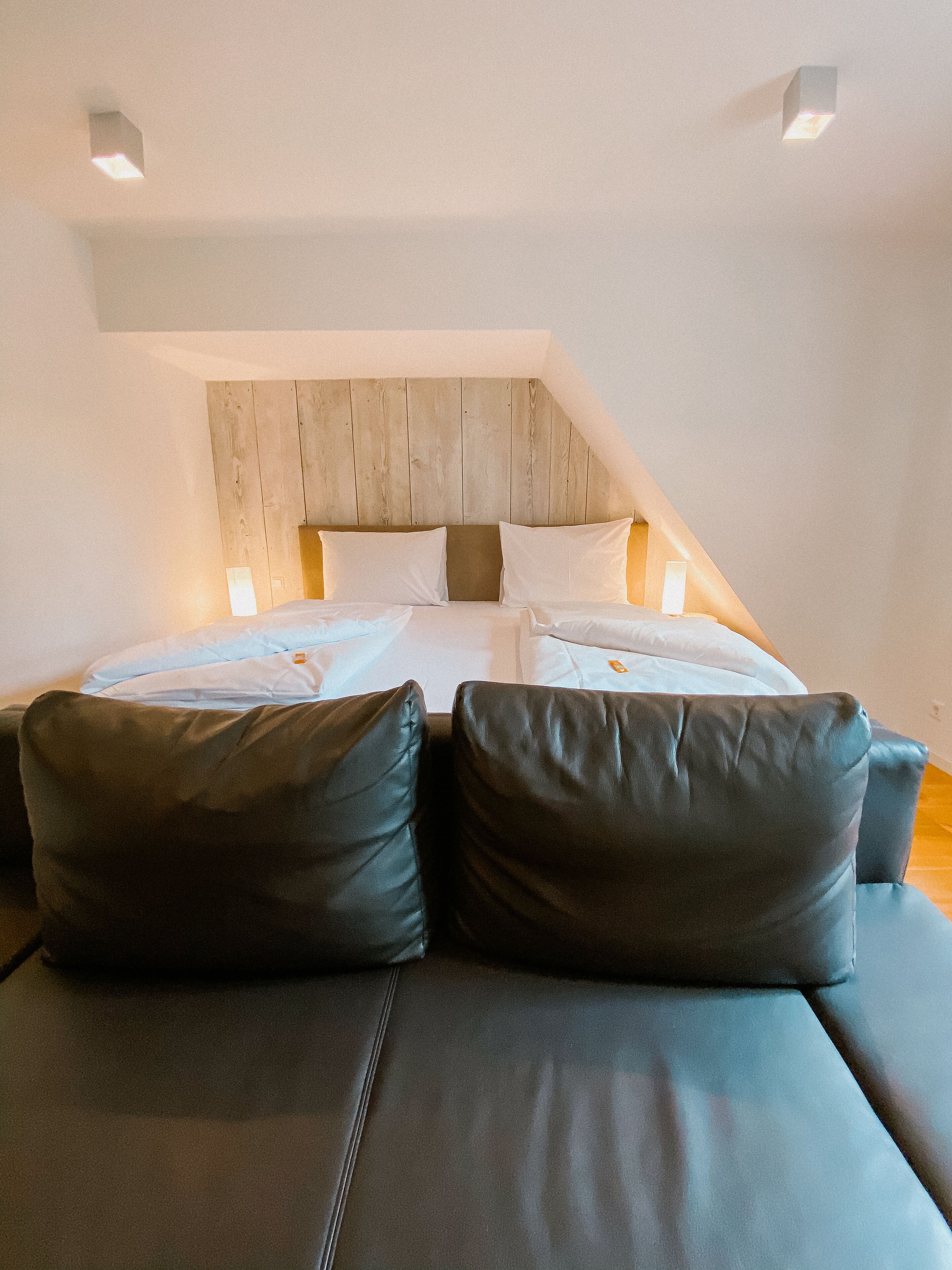 Un dormitorio con cama, dos almohadas, cabecera de madera y un sofá.