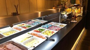 A buffet with various food options, a bar area with bottles, and a wooden wall.