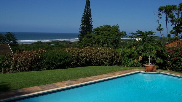 A clear blue swimming pool with a view of the ocean and a well-maintained garden. - Birdcage B and B (Kingsburgh)