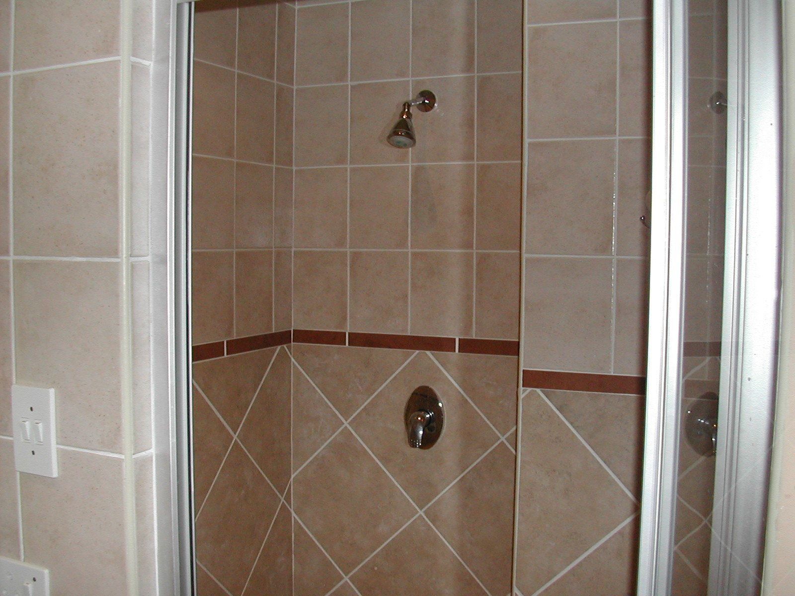 Une douche d’angle, dotée d’un robinet de commande visible et d’un luminaire fixé au mur.