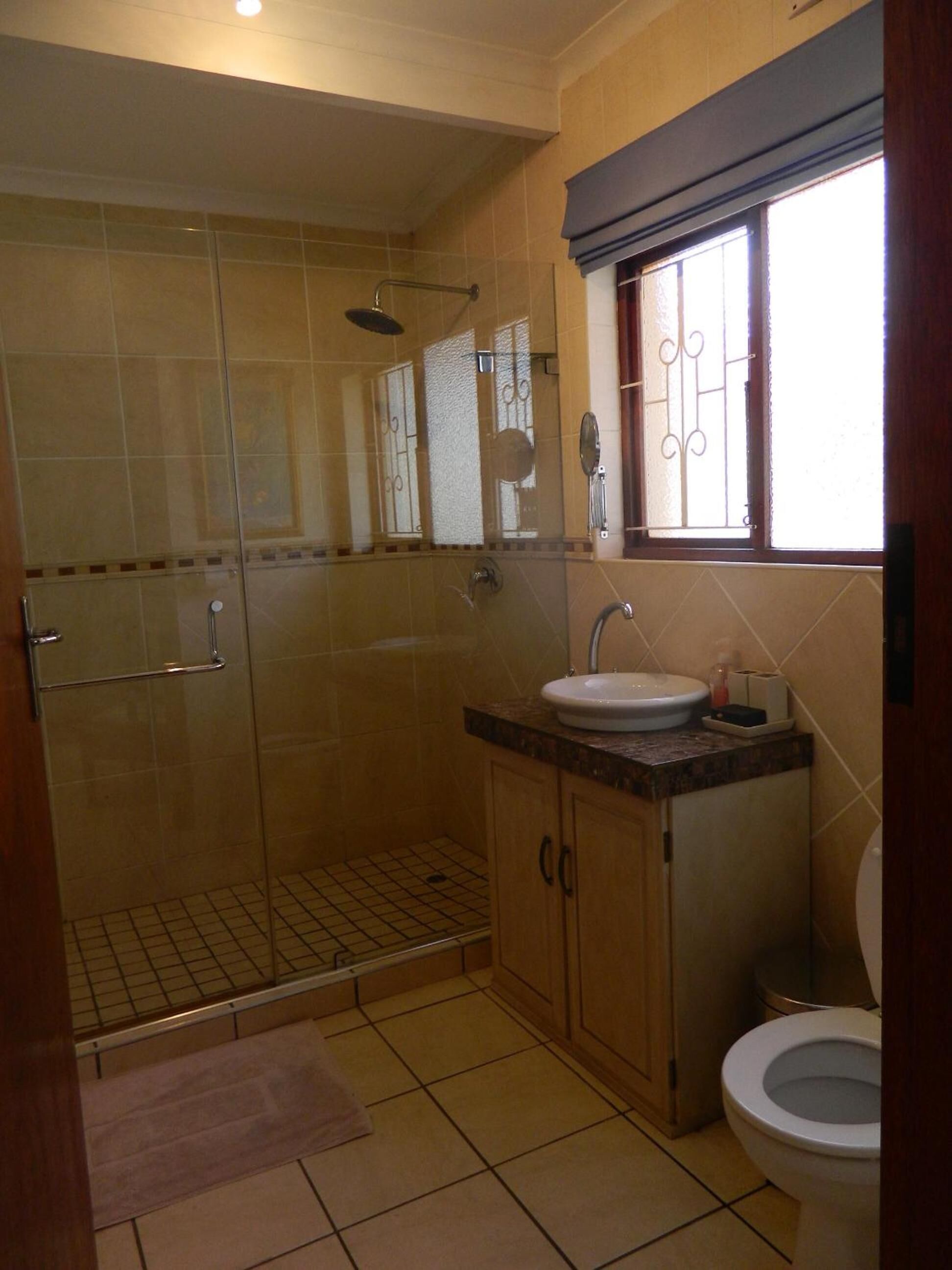 Une salle de bain avec une douche à parois de verre, un lavabo avec un miroir et des toilettes.