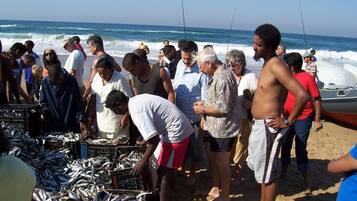Un gruppo di persone in un mercato sulla spiaggia, con pesci esposti in casse.
