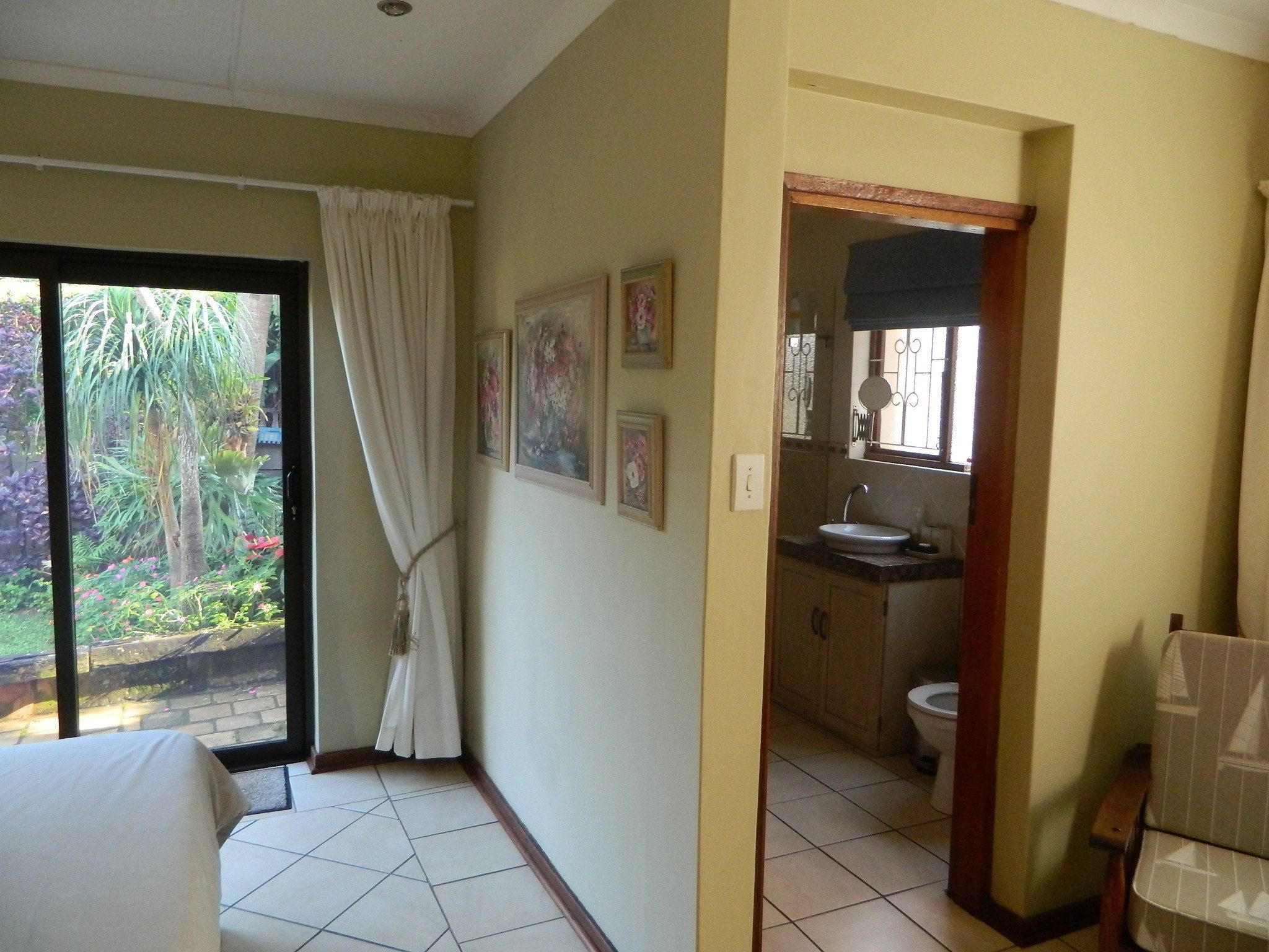 A hotel room with a bed, a bathroom with a sink and toilet, and a view of a garden through a sliding door.