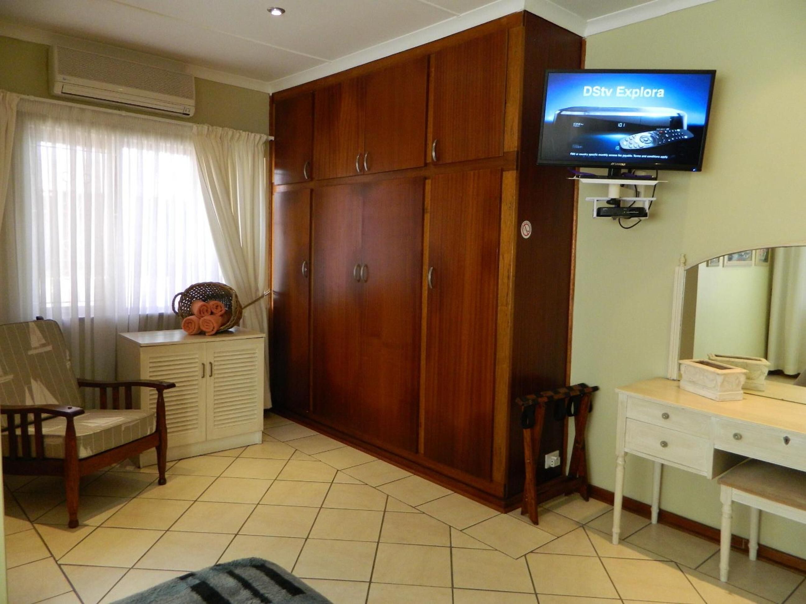 Una habitación con un armario de madera, un televisor montado en la pared, un escritorio con espejo y una silla.