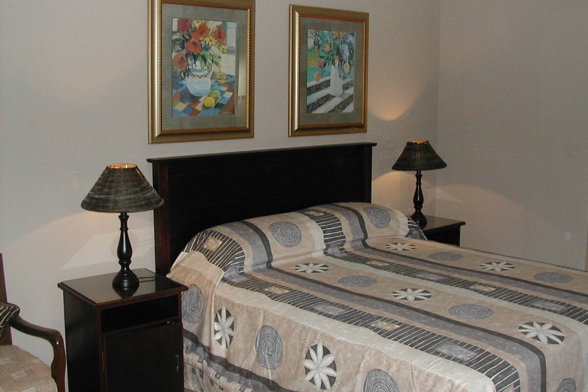 A bedroom with a bed, two bedside tables, two lamps, and two framed artworks on the wall.