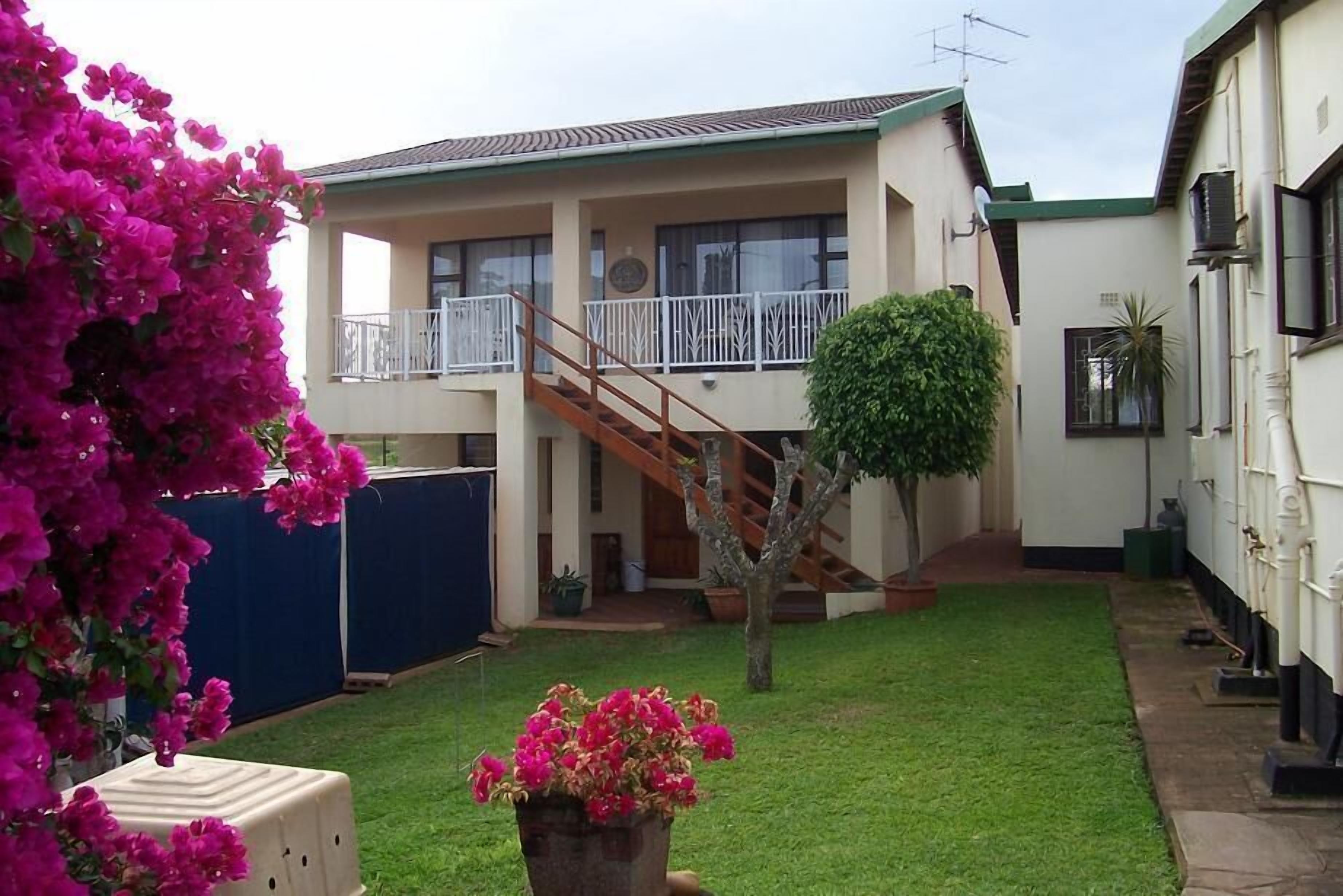 A two-story building with a balcony, a staircase, and a small tree in the yard.