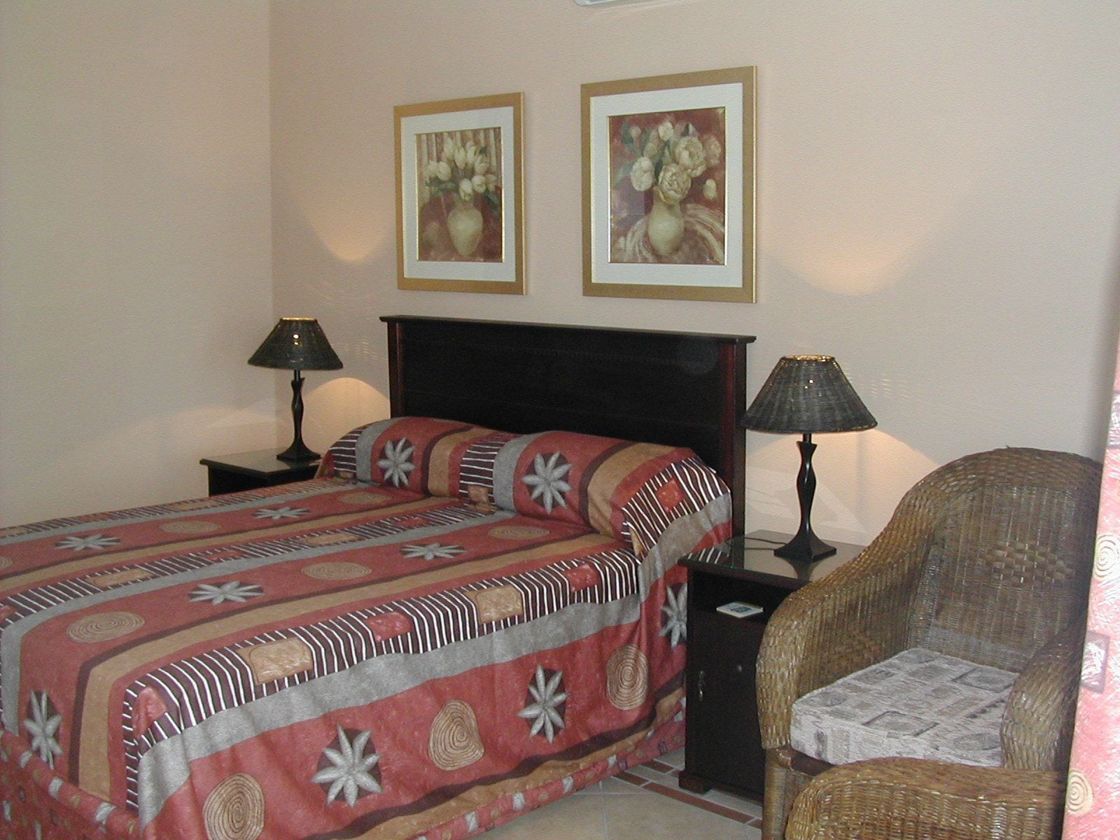 A bedroom with a bed, two bedside lamps, a chair, and two framed floral paintings on the wall.