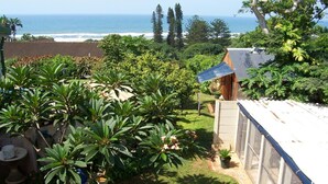A garden with a view of the ocean, a fenced area, and a building with a sloped roof. - Birdcage B and B (Kingsburgh)