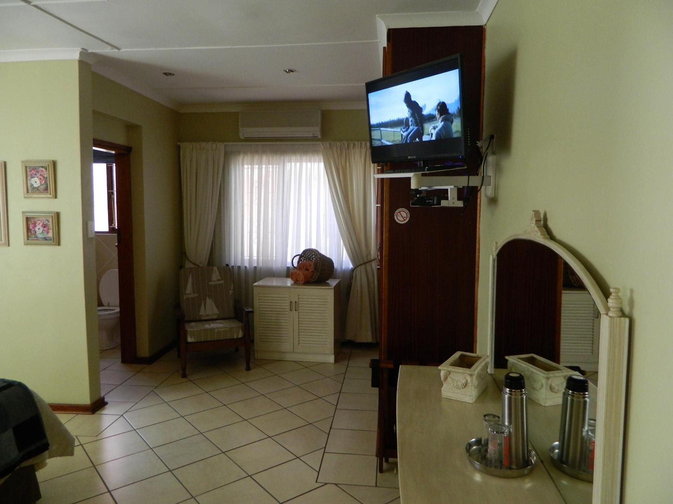 Habitació d'hotel amb televisió, escriptori amb mirall, cadira i finestra amb cortines.