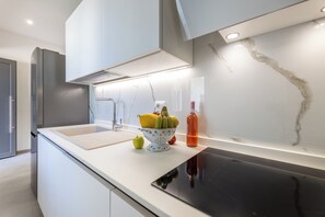 A modern kitchen with a white countertop, a black induction cooktop, a stainless steel refrigerator, and a bowl of fruit.