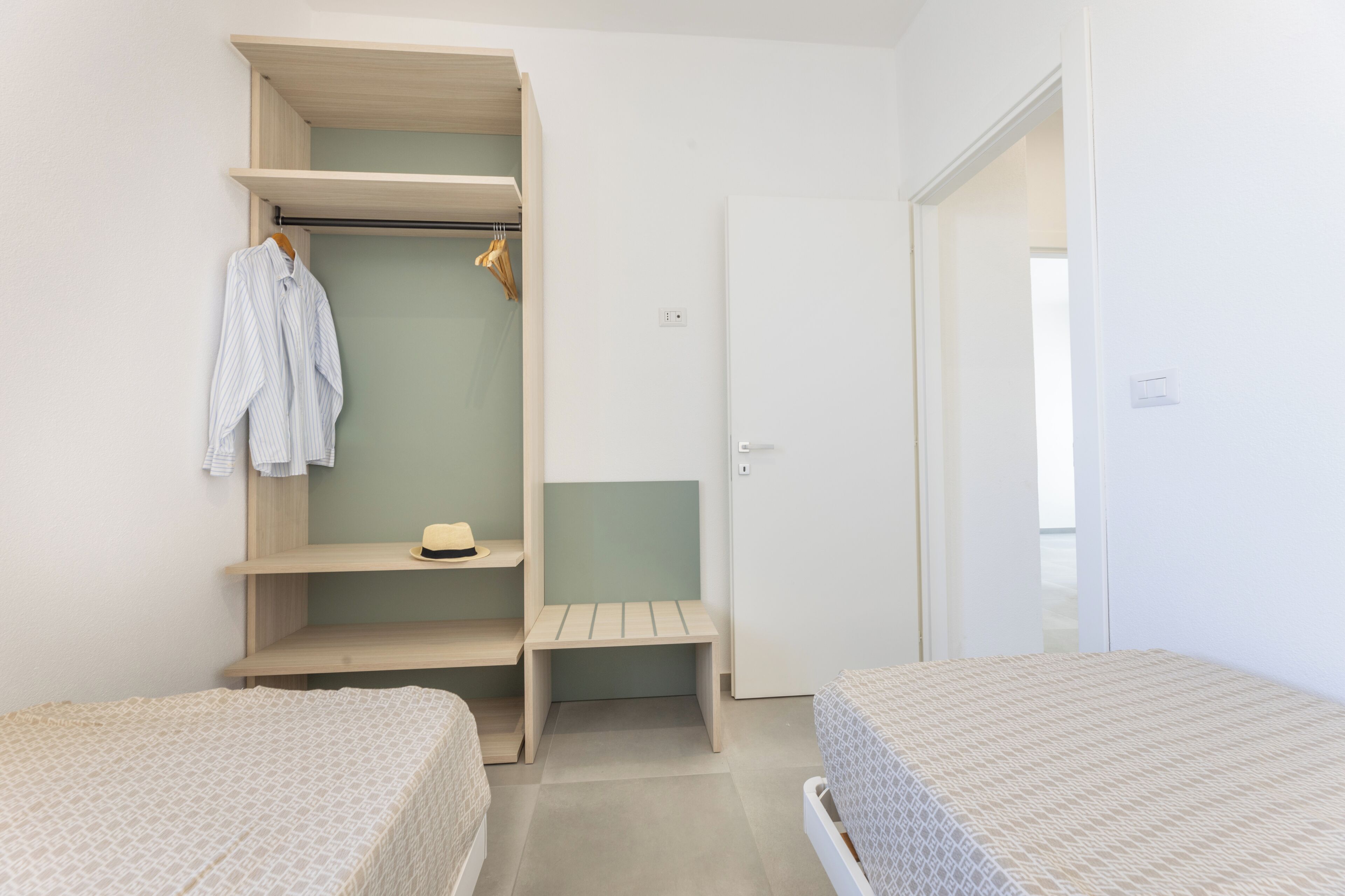 Quarto com duas camas, um guarda-roupa e um banco.