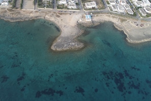 An aerial view of a coastal area with a beach, clear water, and residential buildings. - Appartamenti Mancaversa (Taviano)