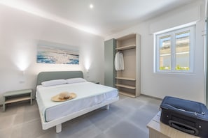 A bedroom with a bed, a bench, a wardrobe, a suitcase, and a window with a view. - Appartamenti Mancaversa (Taviano)