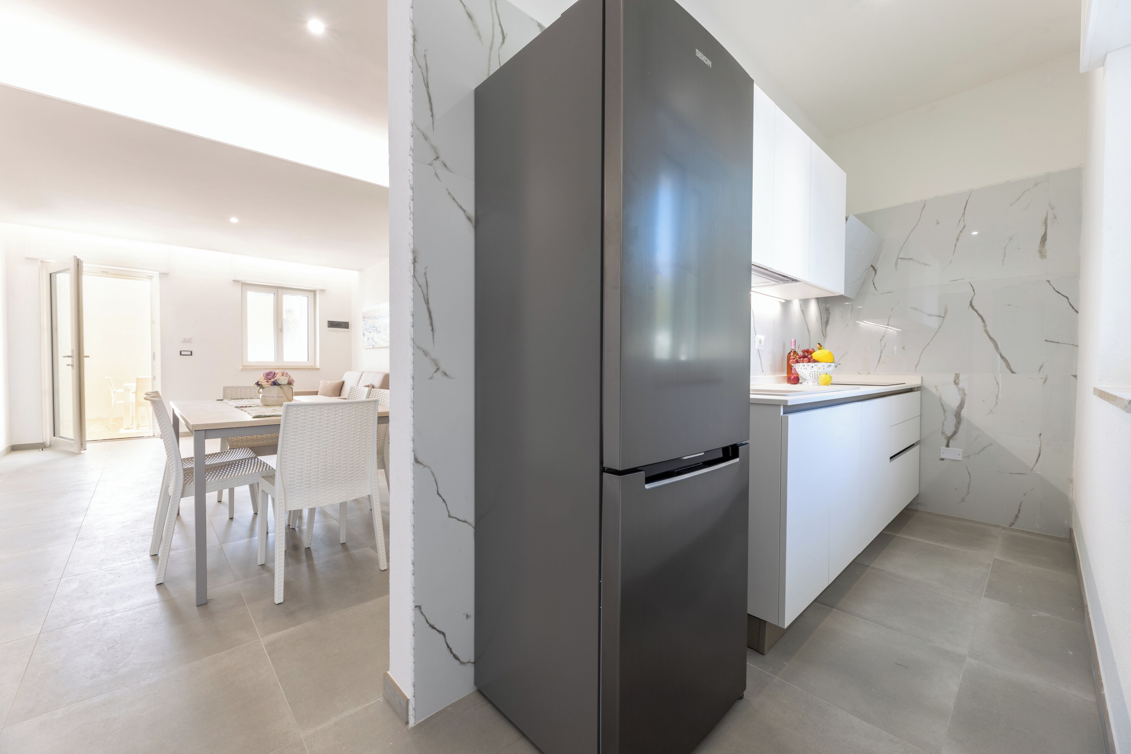 A modern kitchen with a large refrigerator, white cabinetry, and a marble backsplash.