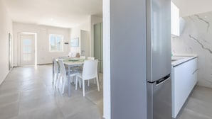 A modern kitchen with a large refrigerator, white cabinetry, and a dining area with a table and chairs.